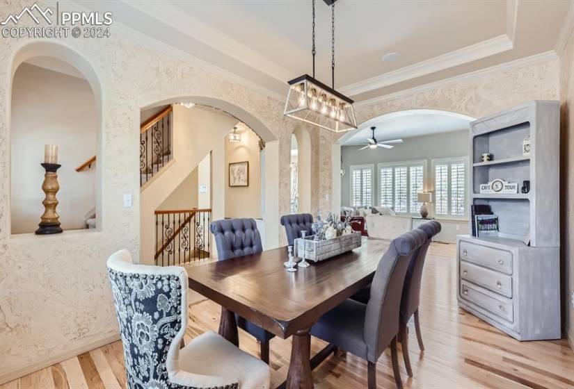 Dining space featuring ornamental molding, ceiling fan with notable chandelier, light hardwood / wood-style flooring, and a raised ceiling