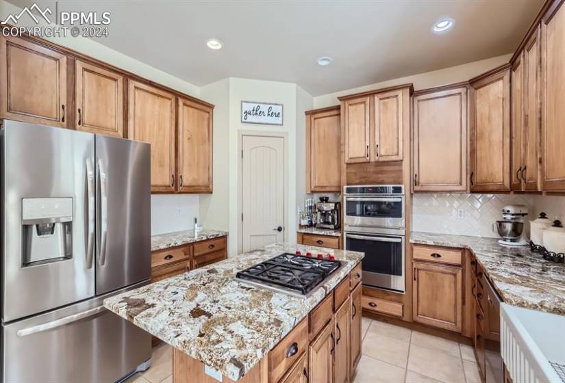 Kitchen with tasteful backsplash, appliances with stainless steel finishes, light tile floors, a kitchen island, and light stone countertops