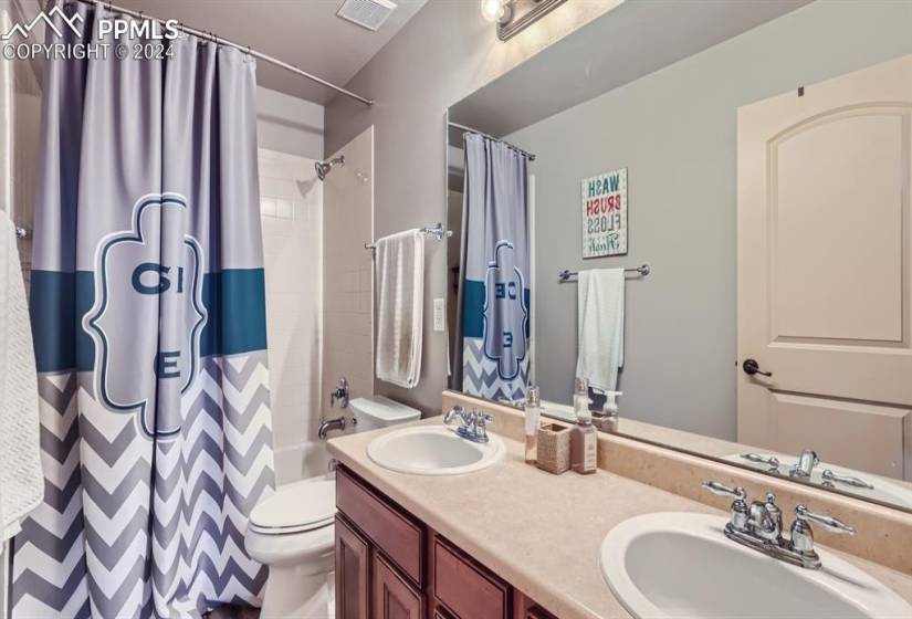 Full bathroom with dual bowl vanity, shower / bath combo with shower curtain, and toilet