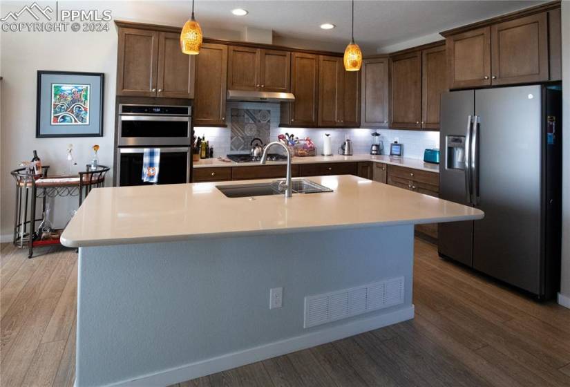 Kitchen featuring appliances with stainless steel finishes, pendant lighting, tasteful backsplash, and a center island with sink