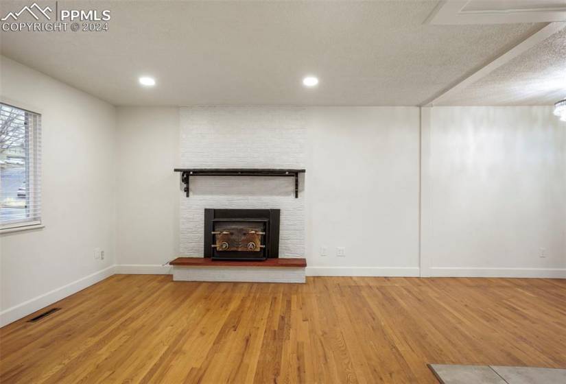 Unfurnished living room with a textured ceiling, a fireplace, light hardwood / wood-style floors, and brick wall