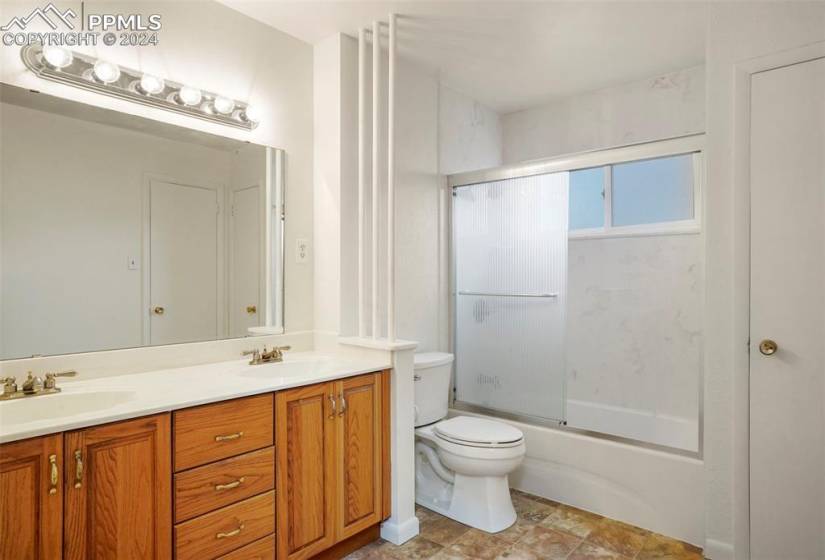Full bathroom featuring enclosed tub / shower combo, double sink, toilet, tile floors, and oversized vanity
