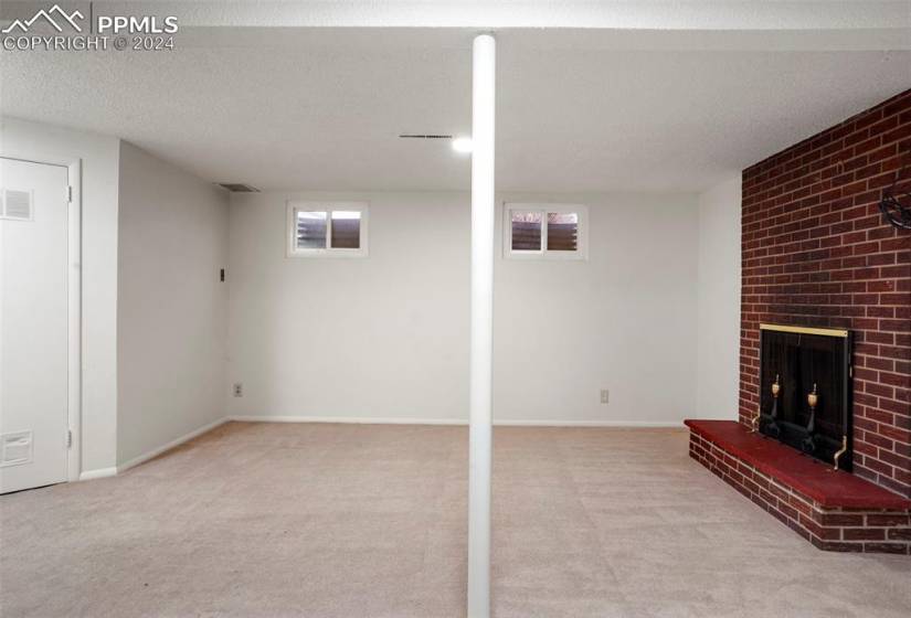 Basement with light colored carpet, a textured ceiling, plenty of natural light, and a brick fireplace