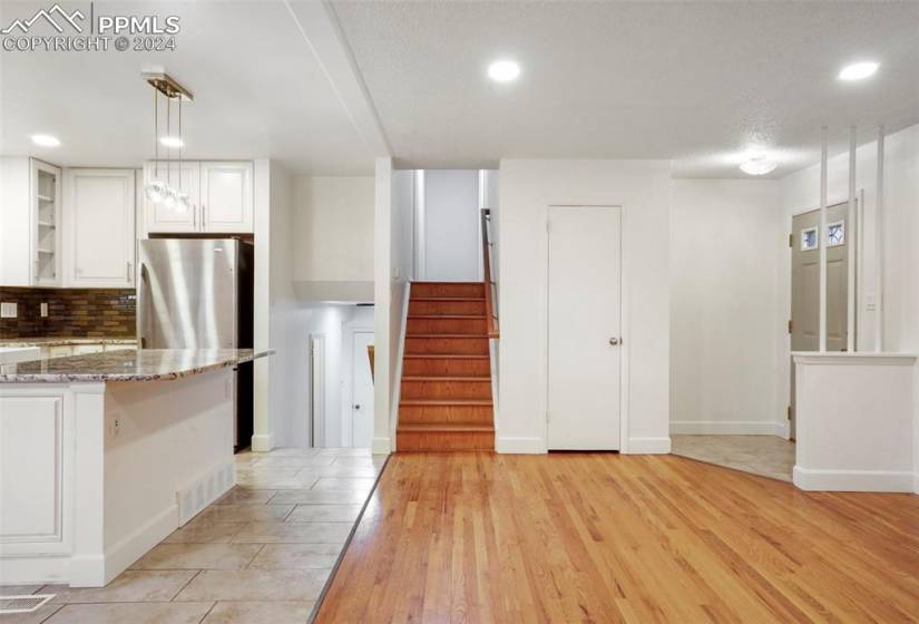 Kitchen featuring tasteful backsplash, light stone countertops, light hardwood / wood-style flooring, hanging light fixtures, and white cabinets