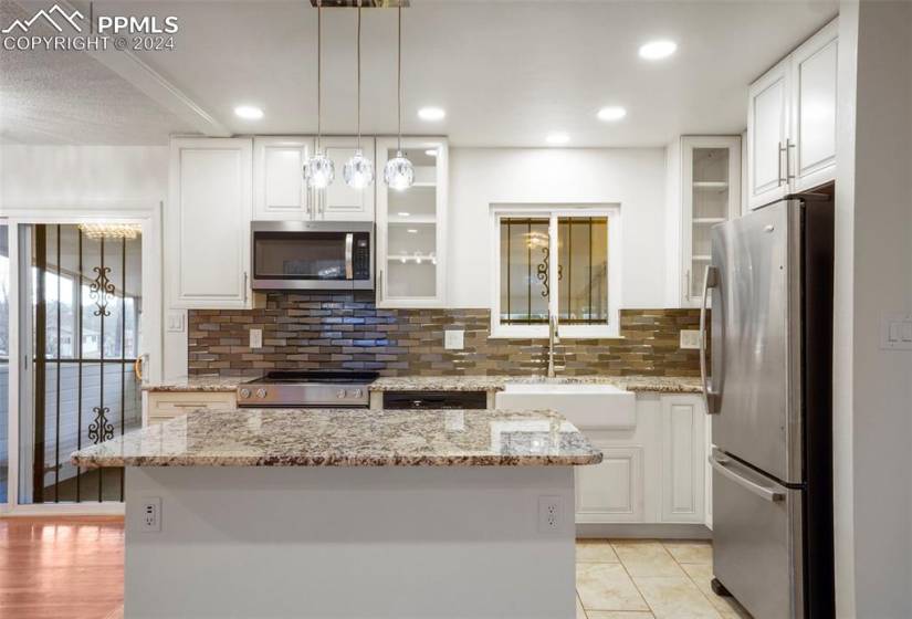 Kitchen featuring backsplash, light tile floors, hanging light fixtures, white cabinets, and stainless steel appliances