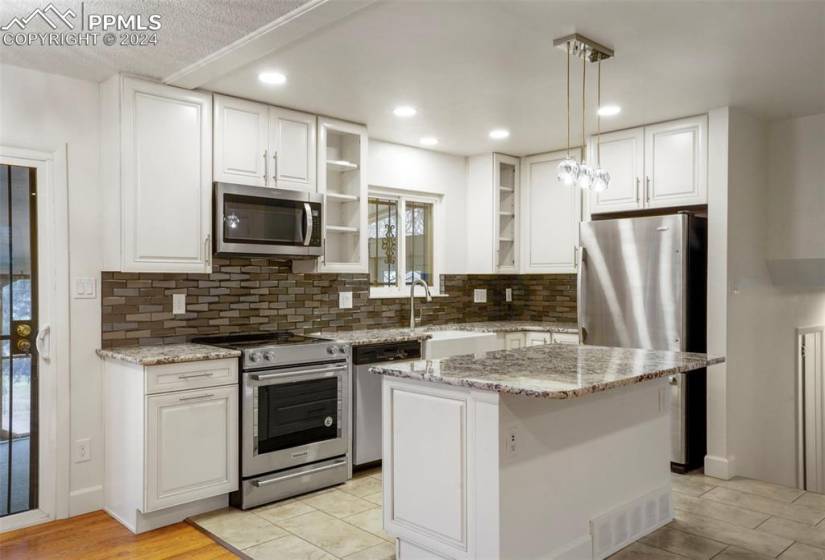 Kitchen featuring white cabinetry, tasteful backsplash, hanging light fixtures, a kitchen island, and stainless steel appliances