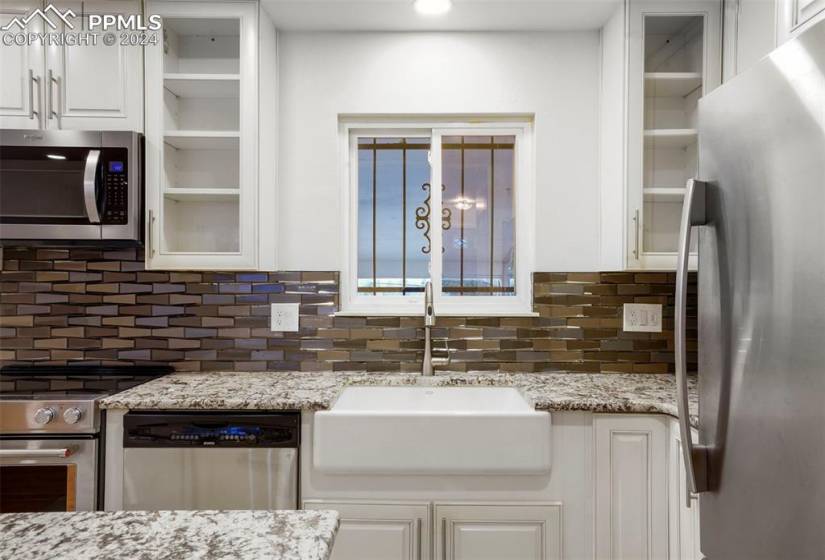 Kitchen featuring appliances with stainless steel finishes, backsplash, white cabinets, and light stone countertops