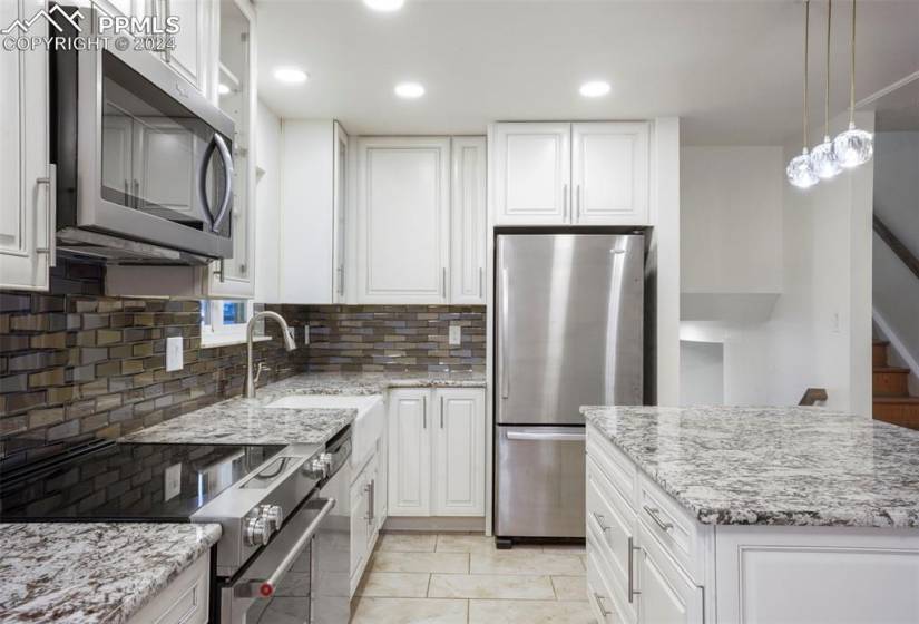 Kitchen with tasteful backsplash, appliances with stainless steel finishes, light tile floors, white cabinets, and decorative light fixtures