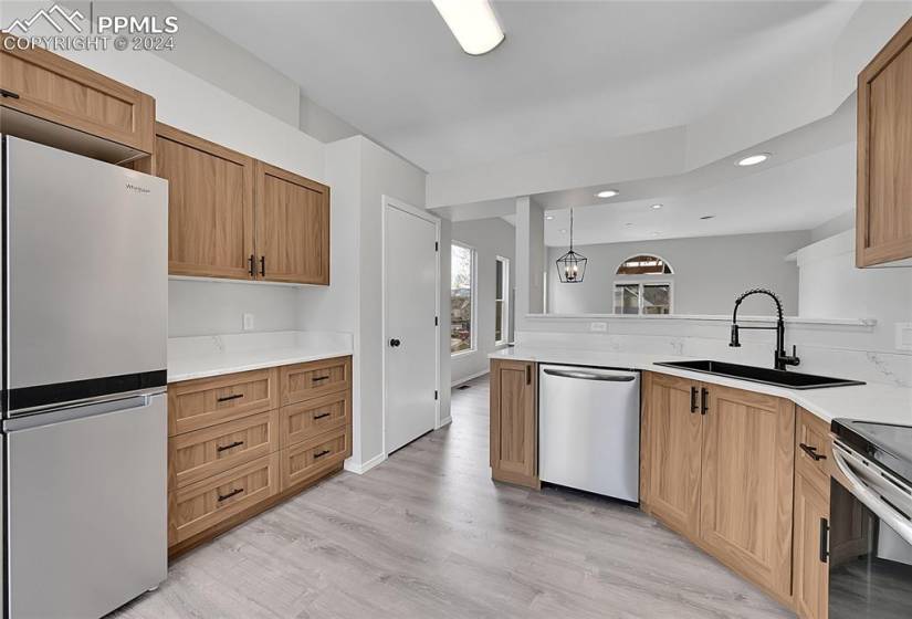 Kitchen with sink, kitchen peninsula, decorative light fixtures, appliances with stainless steel finishes, and light hardwood / wood-style flooring
