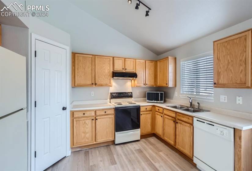 Kitchen with newer lighting, all appliances included, vaulted ceilings, sink, and light wood vinyl flooring