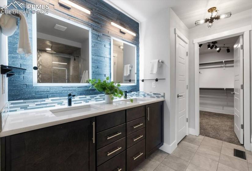 Bathroom with backsplash, dual sinks, walk in shower, vanity with extensive cabinet space, and tile flooring