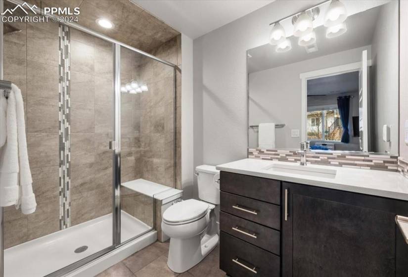 Bathroom featuring vanity with extensive cabinet space, toilet, tile flooring, backsplash, and a shower with shower door
