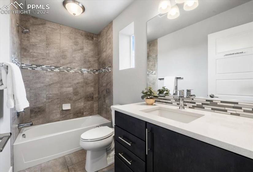 Full bathroom with vanity, tiled shower / bath combo, tasteful backsplash, toilet, and tile floors