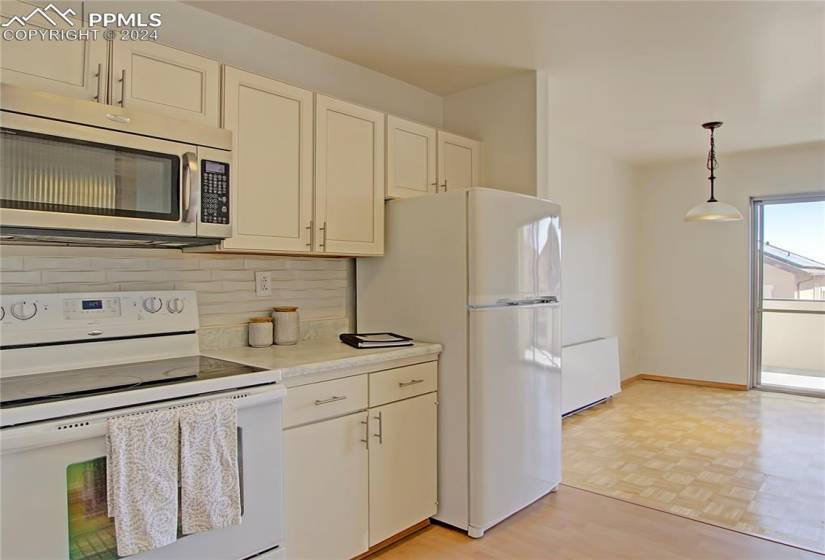 Kitchen with pendant lighting, light hardwood / wood-style floors, cream cabinetry, white appliances, and backsplash