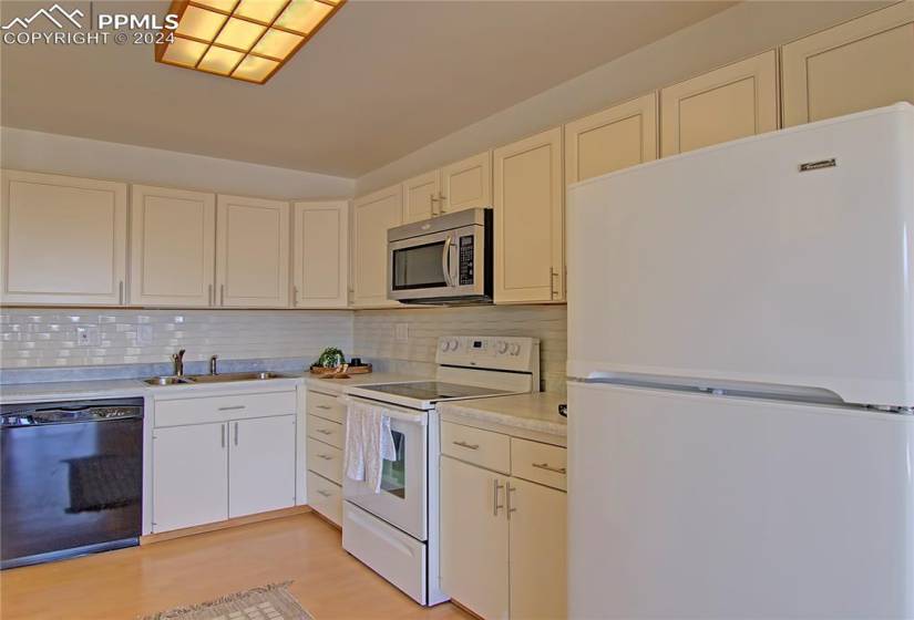 Kitchen featuring light hardwood / wood-style flooring, sink, white appliances, and backsplash