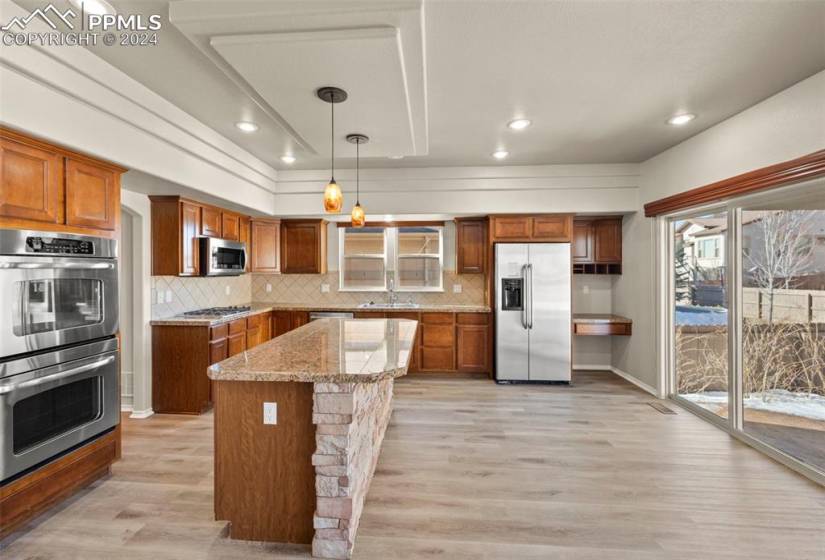 Kitchen with light hardwood / wood-style flooring, stainless steel appliances, tasteful backsplash, and hanging light fixtures
