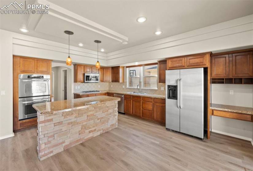 Kitchen with sink, hanging light fixtures, light wood-type flooring, stainless steel appliances, and light stone countertops