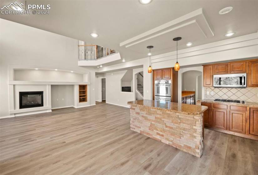 Kitchen with backsplash, stainless steel appliances, light hardwood / wood-style floors, light stone counters, and hanging light fixtures