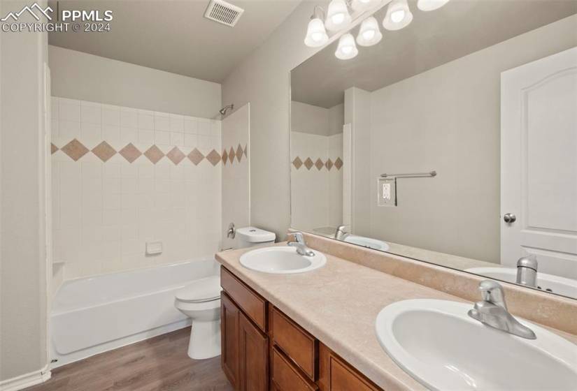 Full bathroom featuring tiled shower / bath, double vanity, hardwood / wood-style floors, and toilet