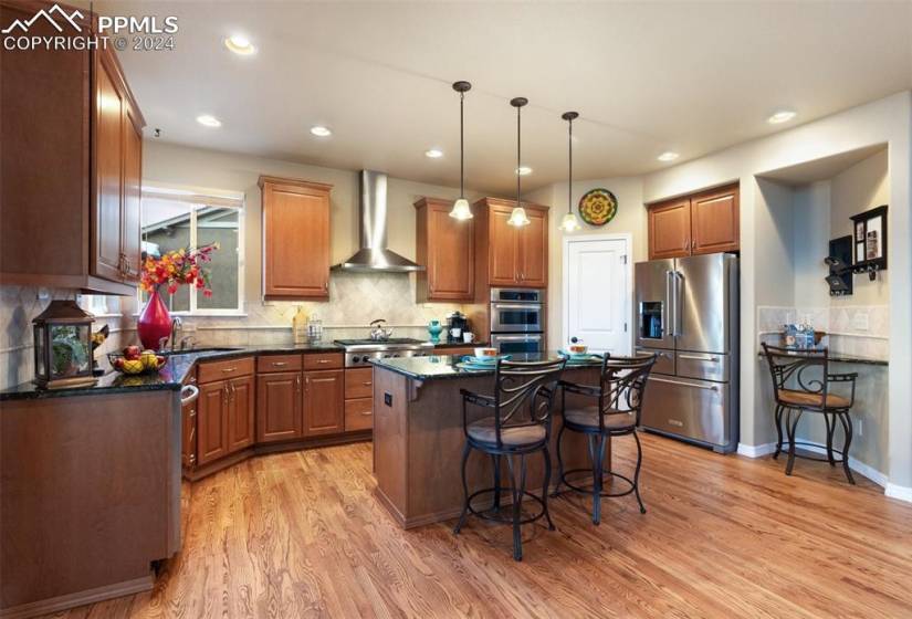 Kitchen featuring tasteful backsplash, a center island, hardwood / wood-style floors, wall chimney range hood, and stainless steel appliances