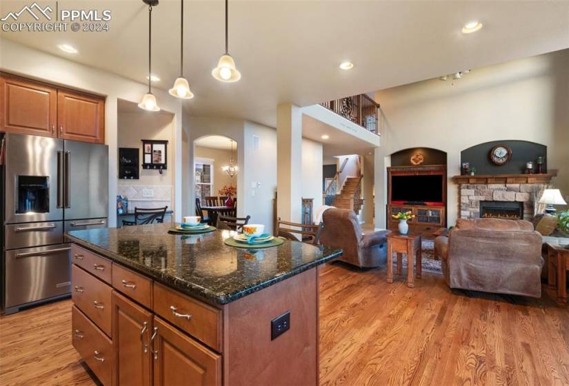 Kitchen with a kitchen island, wood-type flooring, upgraded appliances, stainless steel fridge with ice dispenser, and granite counters
