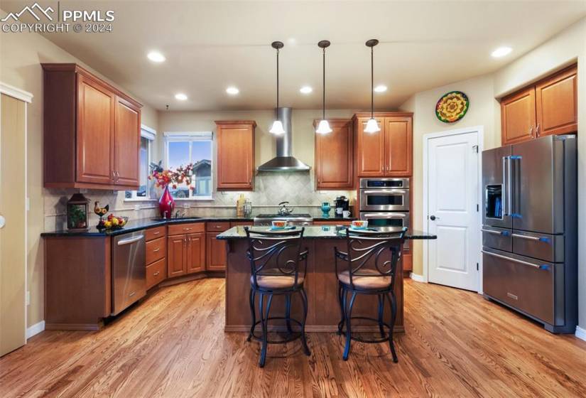 Kitchen with wall chimney exhaust hood, a center island, hardwood / wood-style flooring, and stainless steel appliances