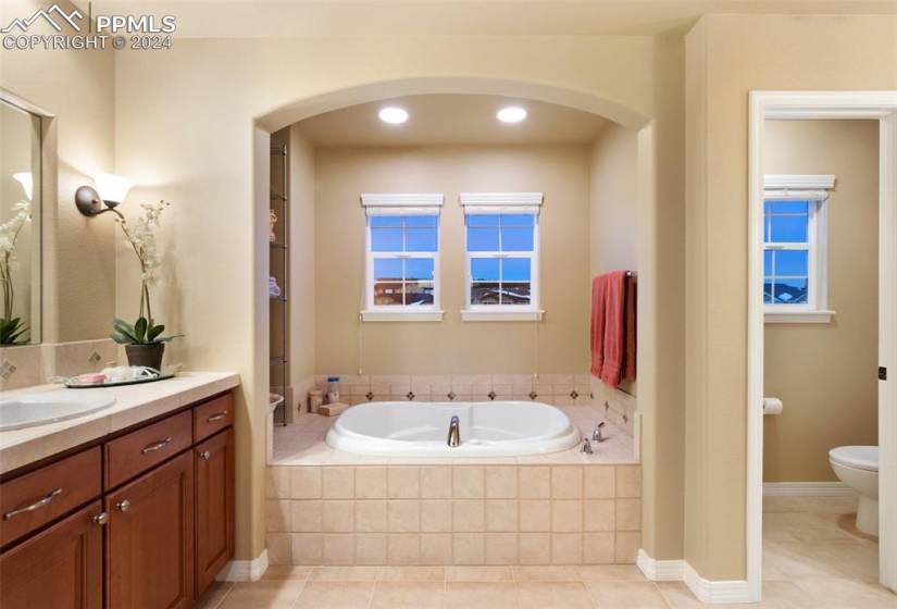 Bathroom featuring tile flooring, tiled tub, toilet, and vanity