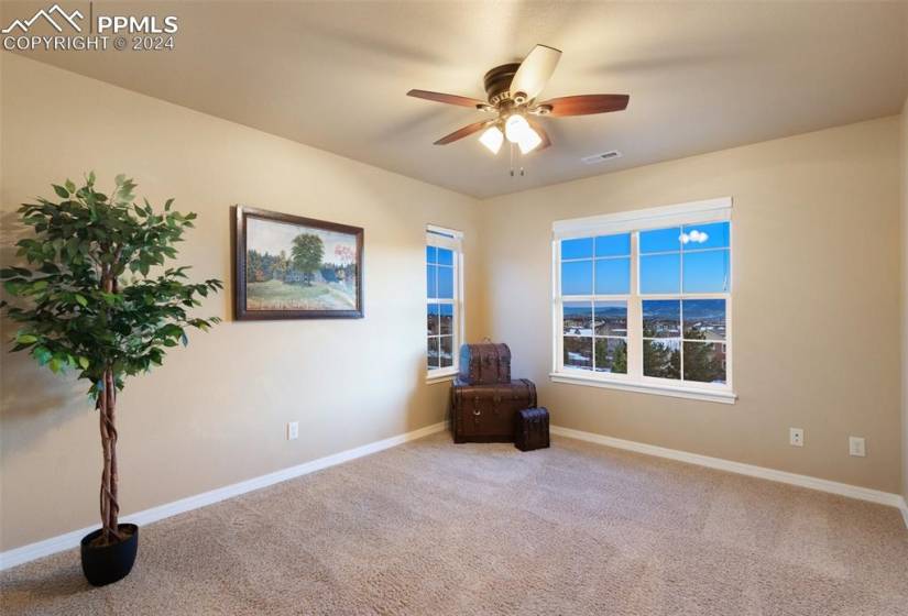 Upper level bedroom with light carpet and ceiling fan and views
