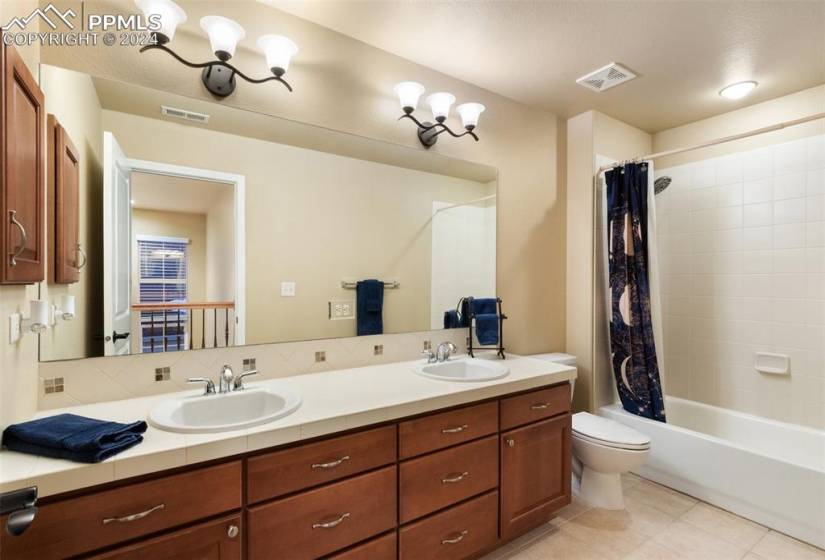 Full bathroom featuring shower / bathtub combination with curtain, toilet, an inviting light fixture, tile flooring, and dual vanity