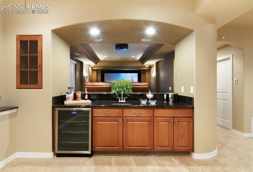 Wet bar area featuring dark stone countertops, beverage cooler, light colored carpet, and sink