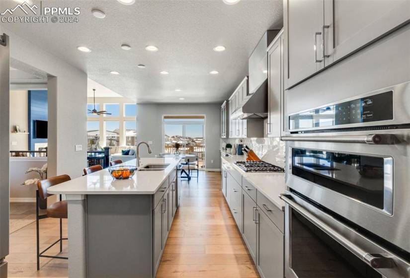 Kitchen featuring tasteful backsplash, stainless steel appliances, light hardwood / wood-style floors, a breakfast bar area, and an island with sink