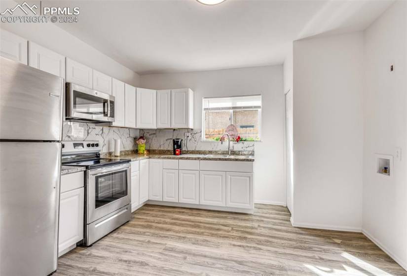 Kitchen with appliances with stainless steel finishes, white cabinetry, and light hardwood / wood-style flooring