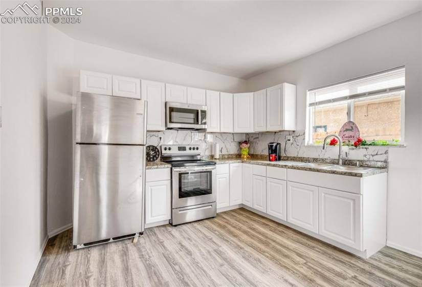 Kitchen with appliances with stainless steel finishes, tasteful backsplash, white cabinets, and light hardwood / wood-style floors