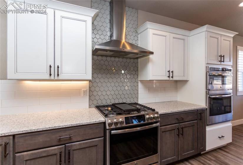 Kitchen with fun backsplash, contrasting cabinets, double ovens and wall chimney exhaust hood