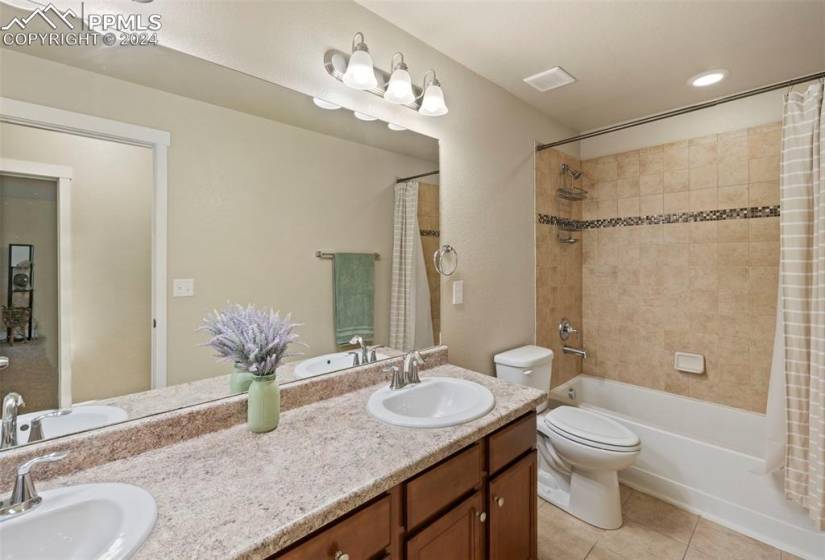 Full bathroom with double vanity, shower / tub combo, toilet, and tile floors