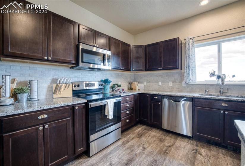 The Kitchen features luxury vinyl plank floors, espresso cabinets with granite countertops, and stainless steel appliances.