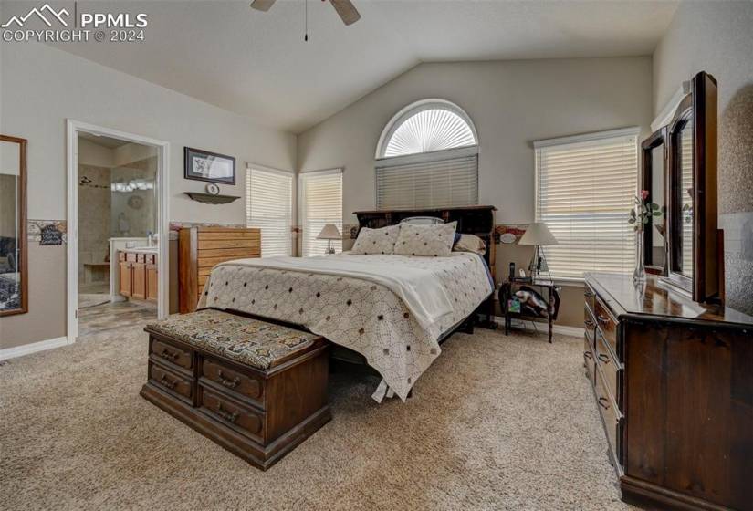 Bedroom with lofted ceiling, light colored carpet, ensuite bathroom, and ceiling fan