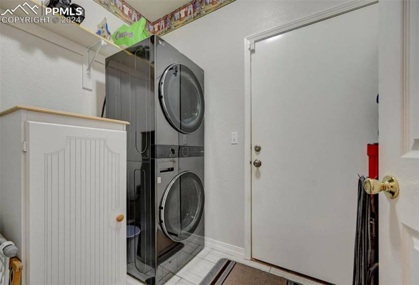 Washroom with stacked washer and clothes dryer and light tile floors