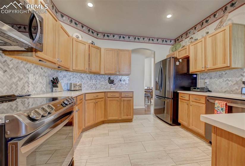 Kitchen with tasteful backsplash, light brown cabinetry, stainless steel appliances, and light tile floors
