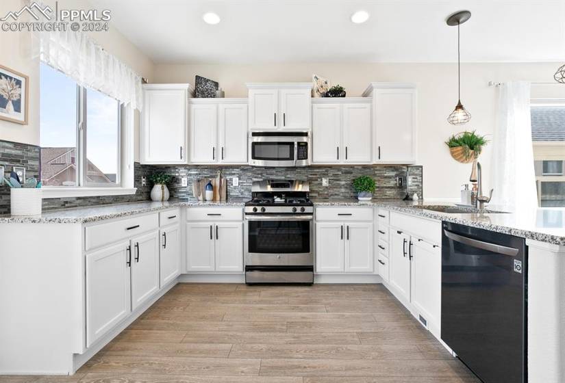 Kitchen with white cabinets, decorative light fixtures, light stone countertops, sink, and appliances with stainless steel finishes