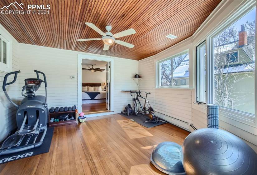 Workout room with wood ceiling, wood walls, ceiling fan, and light hardwood flooring