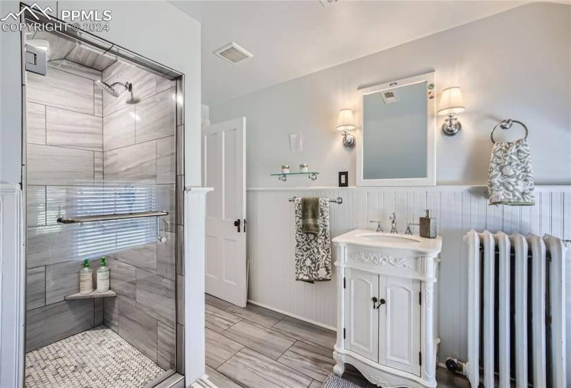 Bathroom with tile floors, vanity, radiator heating unit, and a shower with door