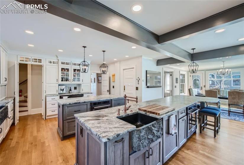 Kitchen featuring light wood flooring, white cabinets, an island with sink, and light stone countertops