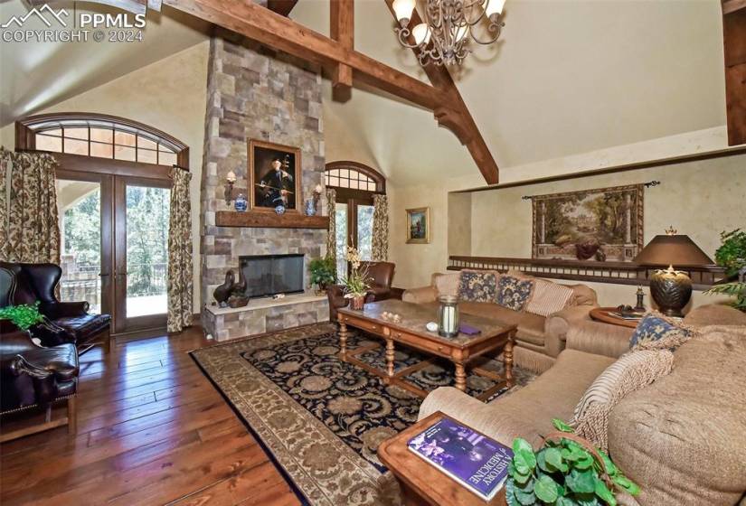Living room with a stone fireplace, a wealth of natural light, a chandelier, and dark hardwood / wood-style flooring