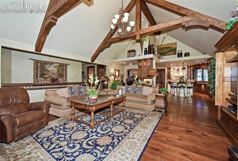 Living room with high vaulted ceiling, a notable chandelier, beam ceiling, and dark wood-type flooring