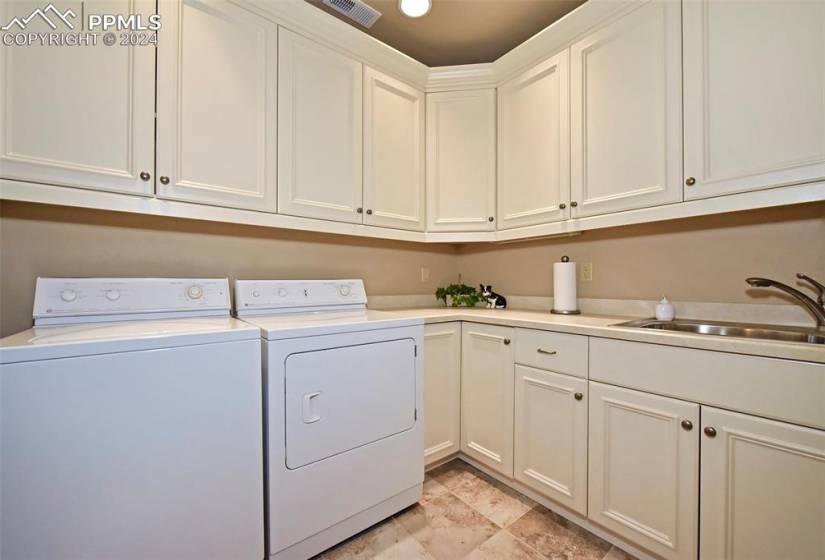 Laundry room with washing machine and dryer, light tile floors, sink, and cabinets