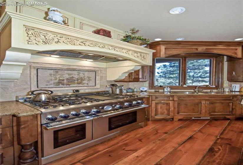 Kitchen featuring backsplash, sink, dark hardwood / wood-style floors, light stone countertops, and double oven range