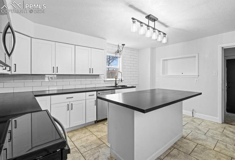 Kitchen featuring hanging light fixtures, white cabinetry, backsplash, sink, and stainless steel appliances