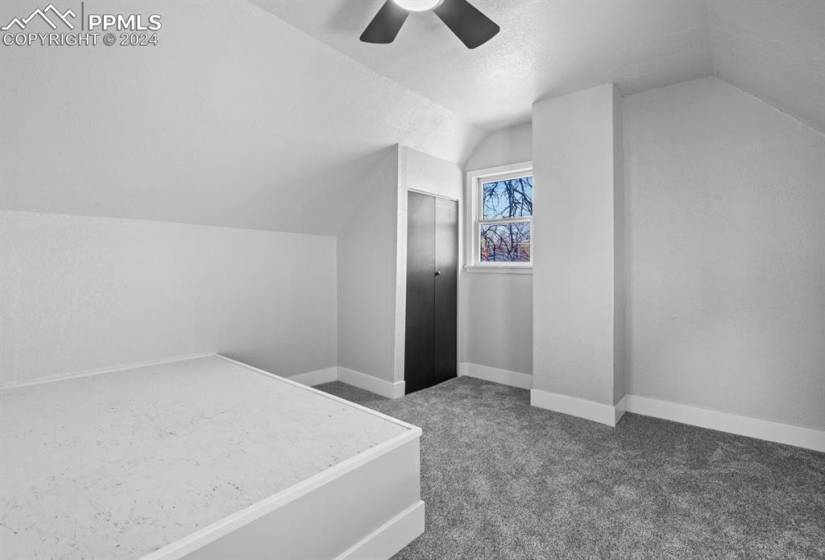 Unfurnished bedroom featuring ceiling fan, dark colored carpet, and vaulted ceiling