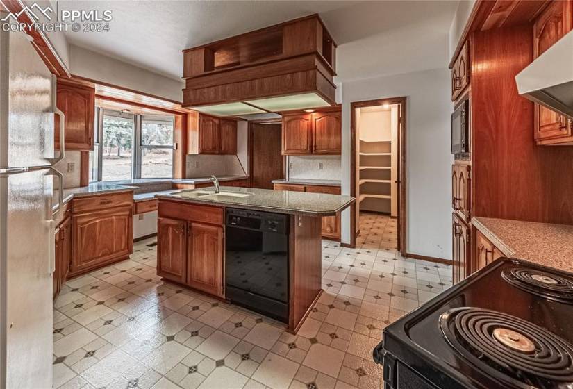 Kitchen featuring a kitchen island with sink, wall chimney exhaust hood, built in microwave, black dishwasher, and white refrigerator